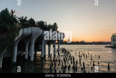 Scenic sunset vista viewed from Manhattan with sun setting over New Jersey, with last sun rays beaming through the Little Island's pillars Stock Photo