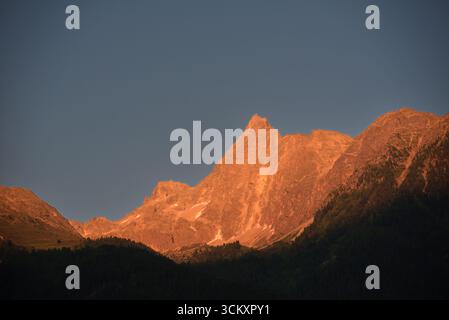 Dramatic alpenglow on a rocky mountain peak at sunset against a deep blue sky in the Alps. Stock Photo