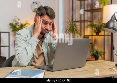 Angry furious man freelancer using laptop while working at home office having nervous breakdown at work, stress management, mental distress problems, losing temper, reaction on failure. Lifestyle Stock Photo