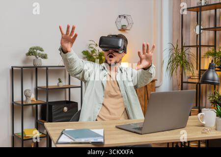 Confident Caucasian man freelancer testing VR headset while sitting at home office table. Young businessman guy making presentation using new gadget d Stock Photo