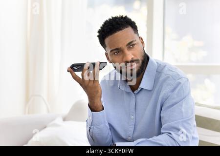 Young male hipster sitting on couch with phone using loudspeaker Stock Photo