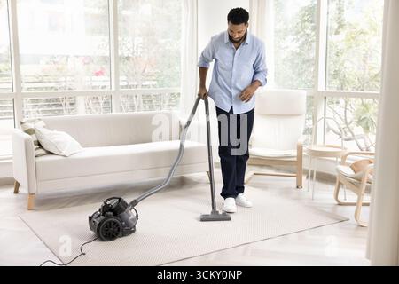Young male vacuuming carpet on floor with washing vacuum cleaner Stock Photo