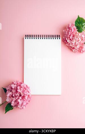 Blank spiral notebook with pink hydrangea flowers on pastel background. Top view, flat lay, mockup. Stock Photo