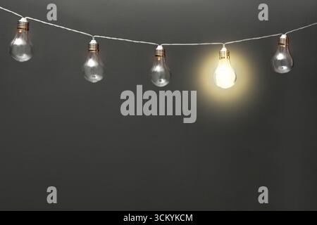 Concept of idea. One glowing light bulb among others against grey background. Space for text Stock Photo