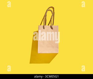 Brown paper shopping bag with handles on vibrant yellow background. Stock Photo