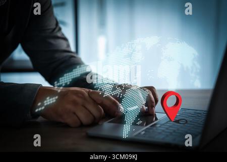 Businessman using laptop with digital world map and red location pin symbol, representing global network, GPS navigation, worldwide connection, and mo Stock Photo