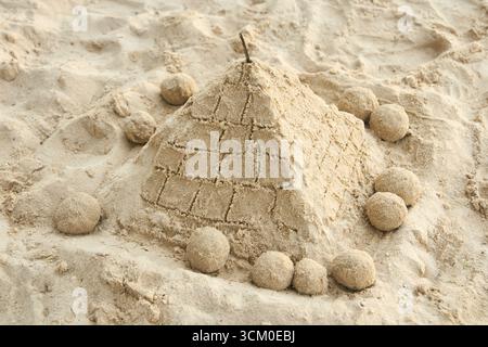 Sand pyramid on beach surrounded by spherical sand sculptures in sunlit setting. Stock Photo
