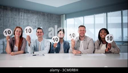 Excited Woman Holding Score Card In Front Of Diverse Committee. Stock Photo