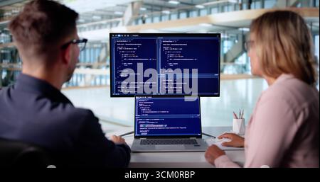 Male Developer Typing Code On Laptop With Female Trainee In Office. Stock Photo