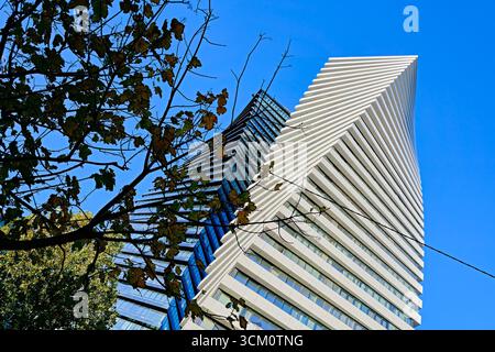 A unique modern building with a wavy facade against a clear blue sky. The composition is complemented by a tree branch, creating a contrast Stock Photo