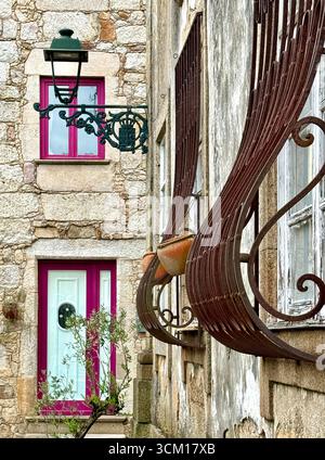 Rustic wrought iron curved security window grille and green streetlight  on a stone wall in historical centre of Barcelos Portugal Stock Photo