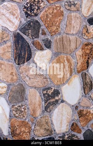 Close-up of a stone wall made from irregularly shaped natural rocks in various earthy tones Stock Photo