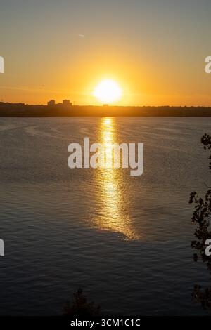 Beautiful sunset view over a calm river with golden sunlight reflecting on the water surface Stock Photo