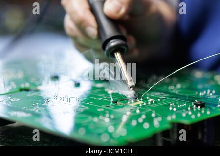 Closeup of technician soldering on a green PCB with visible flux smoke during electronics assembly at a factory workstation Stock Photo