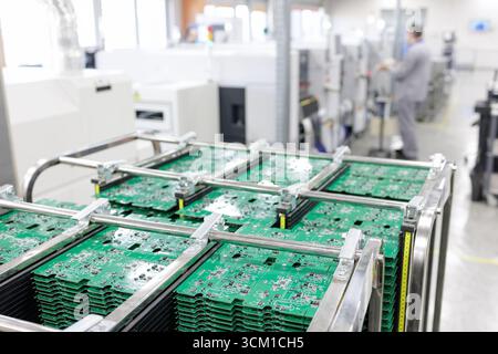 Stacked PCB panels in an ESD rack with technician and SMT equipment in the background on a modern automated electronics production line Stock Photo