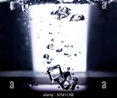 1.Two clear ice cubes plunge into bright illuminated water, releasing hundreds of ascending air bubbles. The high-contrast background accentuates wate Stock Photo