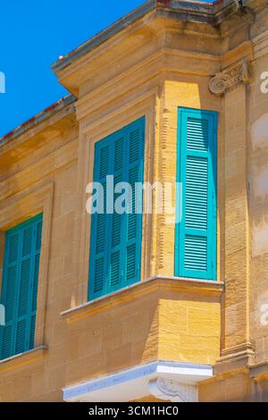 Corner of a light colored stone building is visible in the sun. Windows with bright turquoise shutters. Detailed view of traditional window shutters i Stock Photo