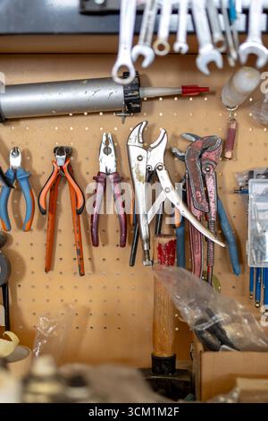 A wall of tools in an artisan workshop, with pliers and wrenches hanging on a pegboard. The image represents manual labor, craftsmanship, and DIY. Stock Photo