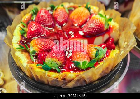 Strawberry cheesecake topped with whole strawberries & caramel jam, on black plate with fresh leaves, creamy dessert perfect for street food concept. Stock Photo