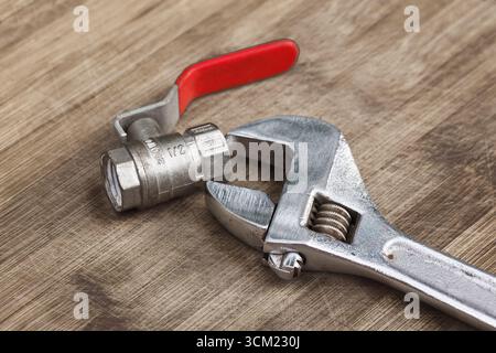 Adjustable wrench and 1/2 inch water tap on a wooden board Stock Photo