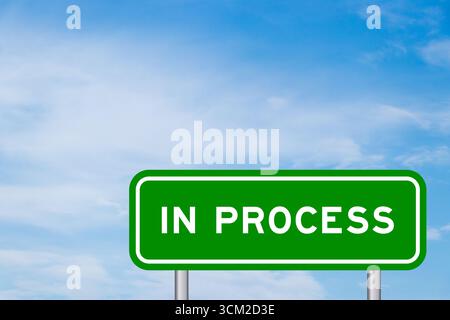 Green color transportation sign with word in process on blue sky with white cloud background Stock Photo