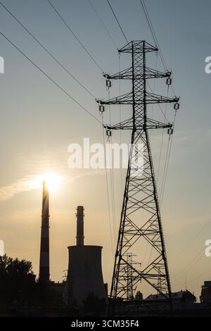 High voltage power lines and industrial plant with chimneys at sunset, symbolizing importance of reliable electricity infrastructure Stock Photo