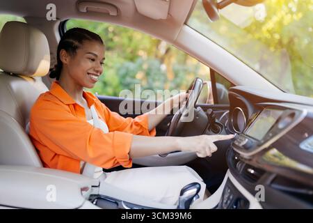 Smiling African American woman in car using touchscreen display, adjusting navigation Stock Photo