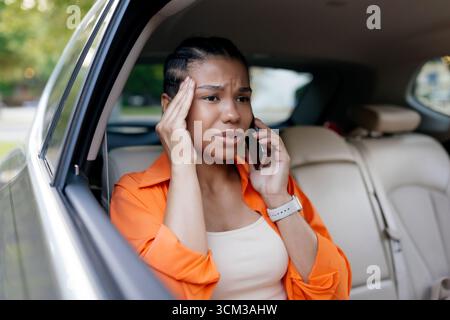 Concerned African American woman in car talking on phone with stressed expression Stock Photo