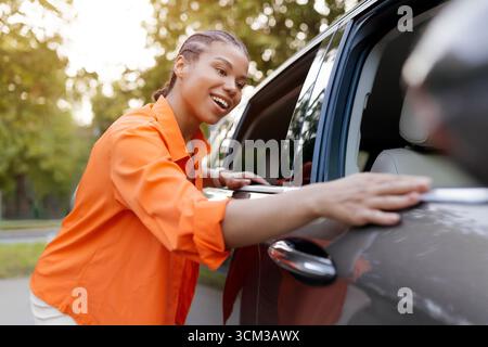 Smiling African American woman leaning on car, enjoying cheerful outdoor moment Stock Photo
