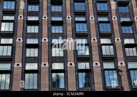 A facade of a building composed of many windows set within dark panels and vertical bands of lighter stone  in London, UK. Stock Photo