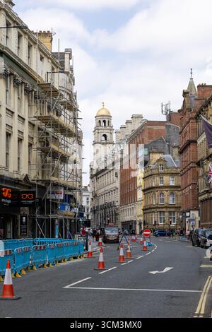 A street scene features ornate architecture, scaffolding, traffic cones, and pedestrians under a cloudy sky  in Liverpool, UK. Stock Photo