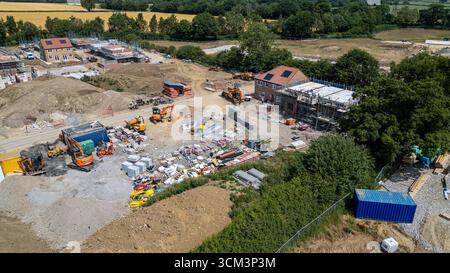 Aerial view of a residential construction site with multiple houses under various stages of development. Excavators, building materials, and shipping Stock Photo