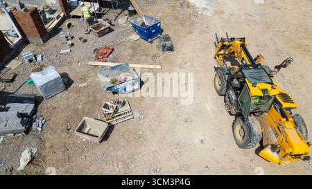 An aerial view of a construction site showing a telehandler, stacks of bricks and blocks, wheelbarrows, and a worker  at Miller Homes in Catterick, UK Stock Photo