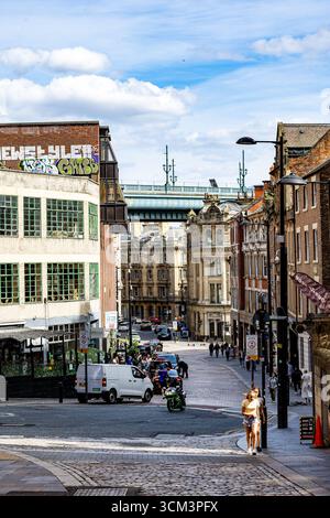 A sunlit street scene with vintage architecture, a bridge in the distance, and various vehicles and pedestrians  in Newcastle upon Tyne, UK. Stock Photo