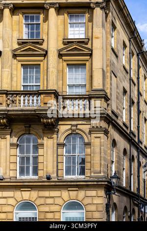 A close-up view of a tan stone building's corner facade featuring multiple windows of various shapes and sizes, a decorative balcony, and architectura Stock Photo