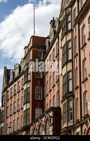 A side view of tall, red brick buildings with numerous windows under a cloudy blue sky, featuring architectural details like bay windows and dormers Stock Photo