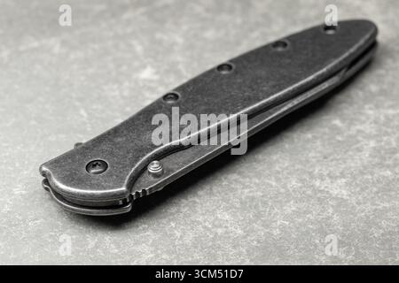 High detail image of a sleek black foldable pocket knife against a solid gray surface. Great for concepts of tools, outdoor gear, or vintage-style obj Stock Photo