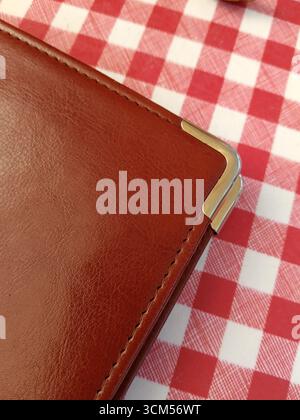 A brown leather wallet is on a red and white checkered cloth Stock Photo