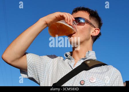 A young man drinking a pint of lager from a plastic cup Stock Photo