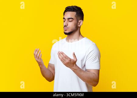 Religious young arab man praying on yellow background, copy space Stock Photo