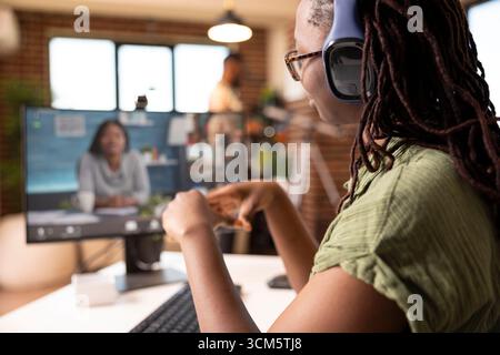 African american woman entrepreneur seated at desk, attending online business workshop from home. Focused female freelancer working remotely and developing new strategies with virtual team. Stock Photo