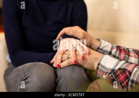 Close up of young white couple holding hands on sofa, showing emotional connection during marriage counseling. Caucasian man and woman supporting each other in therapy session. Stock Photo