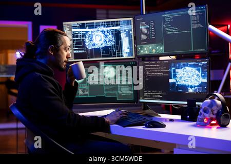 Hacker drinking coffee, installing spyware with AI to secretly gather data about user activity. Rogue engineer enjoying beverage, coding exploits using deep learning to gain unauthorized access Stock Photo