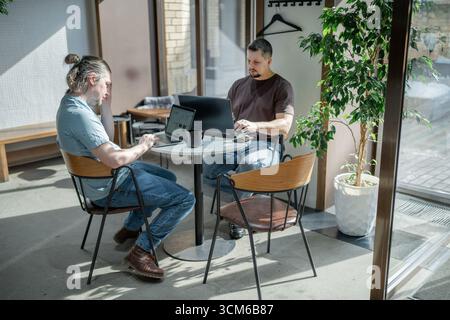 Programmers discussing over laptop working at startup. Office, business and friends together in teamwork with notebook, laptop and coffee workplace Stock Photo