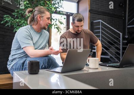 Programmers discussing over laptop working at startup. Office, business and friends together in teamwork with notebook, laptop and coffee workplace Stock Photo