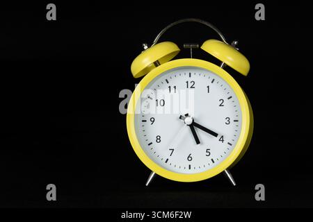 Close up to a classic analog yellow alarm clock at the right side with black background Stock Photo