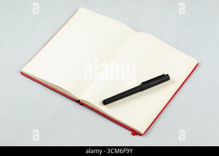 close up to a red blanked notebook with a black pen over its right sheets Stock Photo