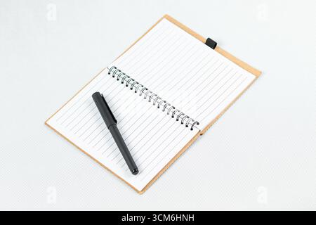 close up to a blanked notebook with a white lined sheets and a black pen over the left sheet and a white background Stock Photo