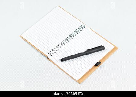 close up to a blanked notebook with a white lined sheets and a black pen over the right sheet and a white background Stock Photo