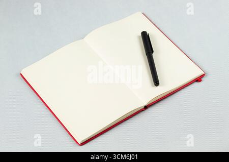 close up to a red blanked notebook with a black pen over its right sheets and a white background Stock Photo